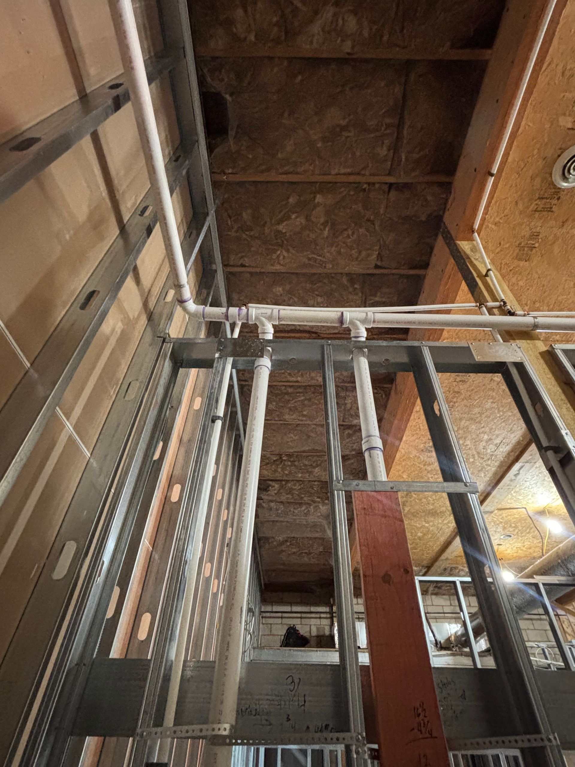 Construction view: metal stud framing with white pipes along ceiling.