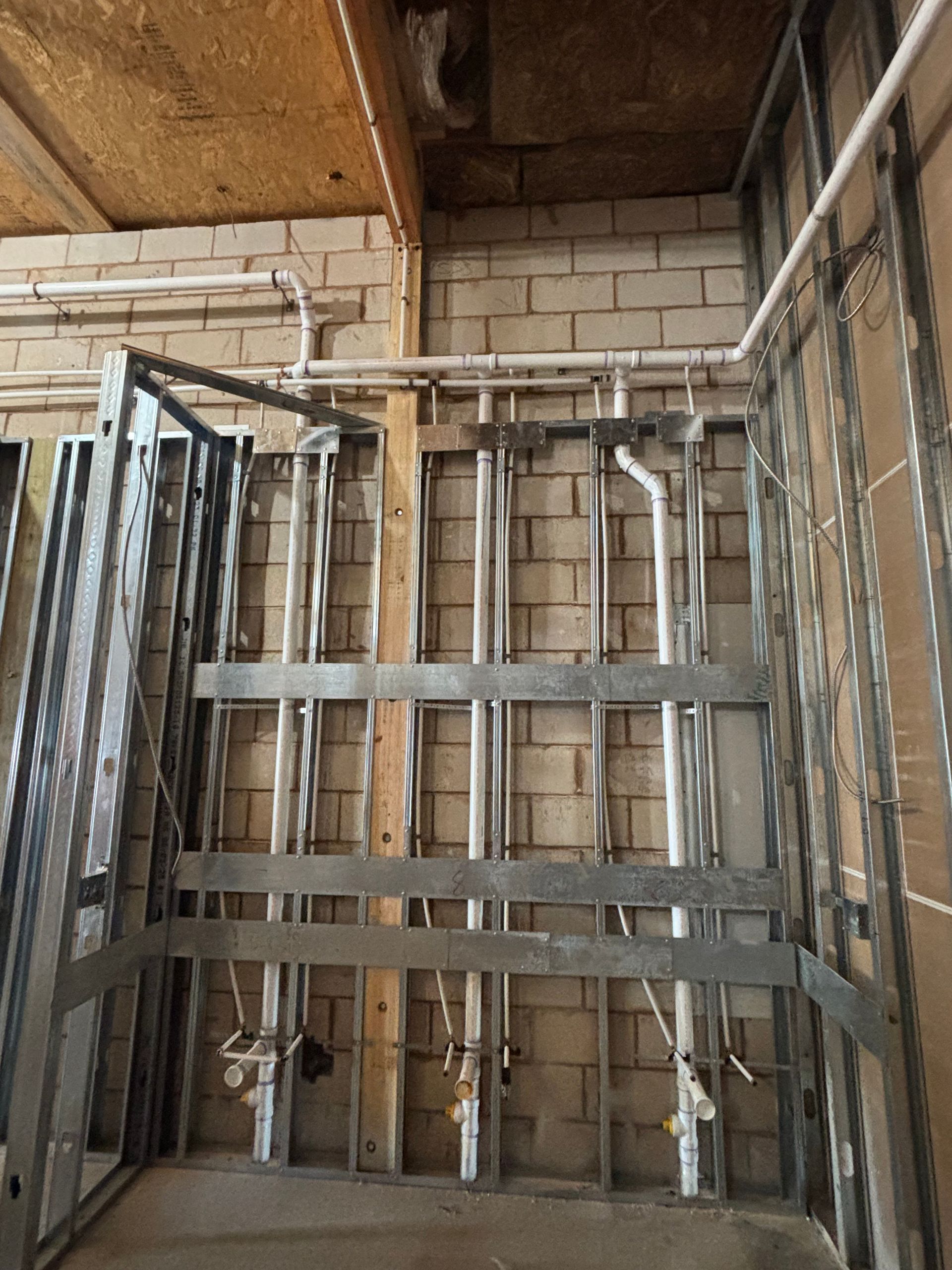 Metal framing with plumbing pipes against a brick wall, ready for drywall.