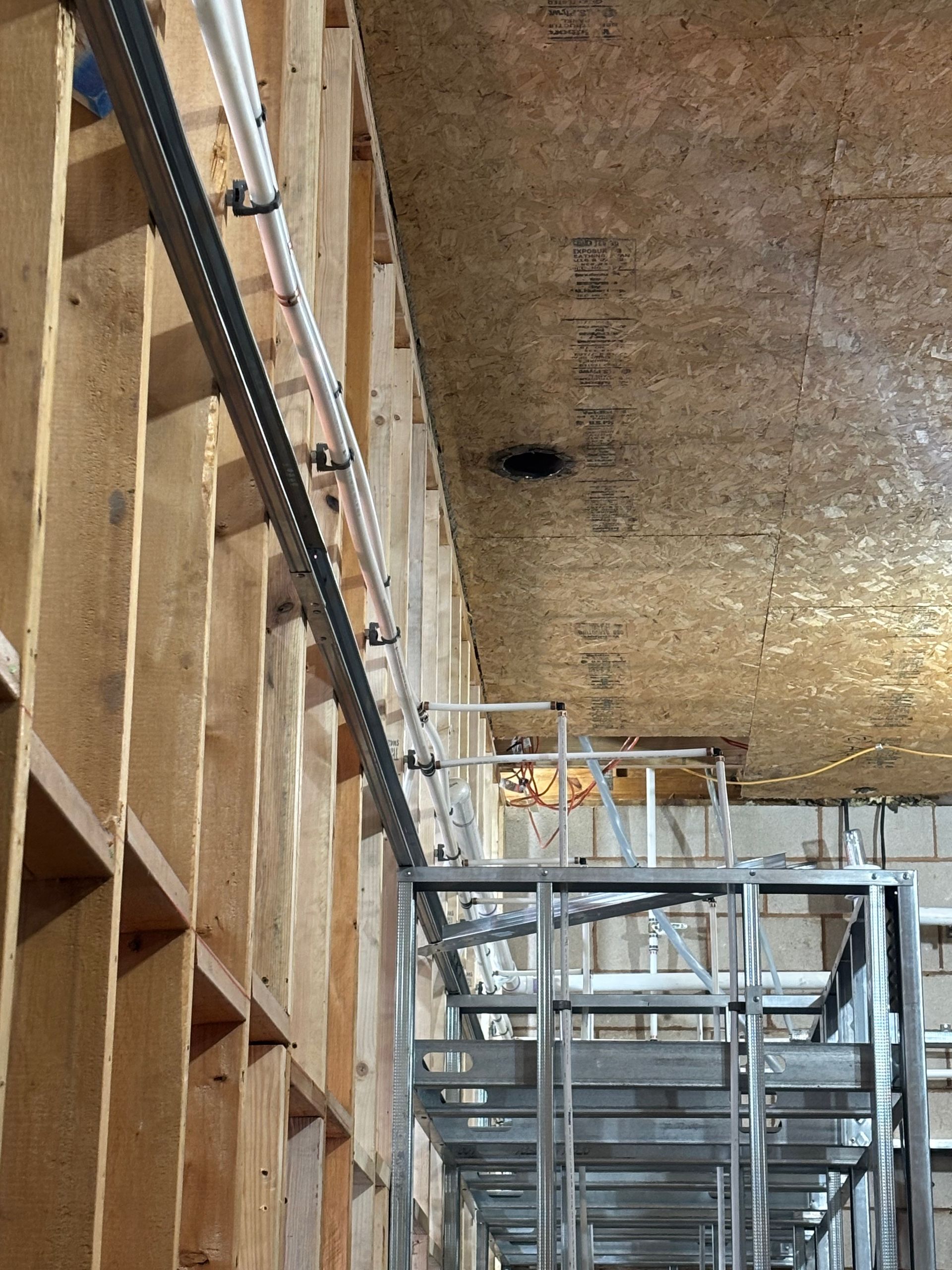 Interior wall with exposed wooden studs, metal electrical conduit, and metal framework.