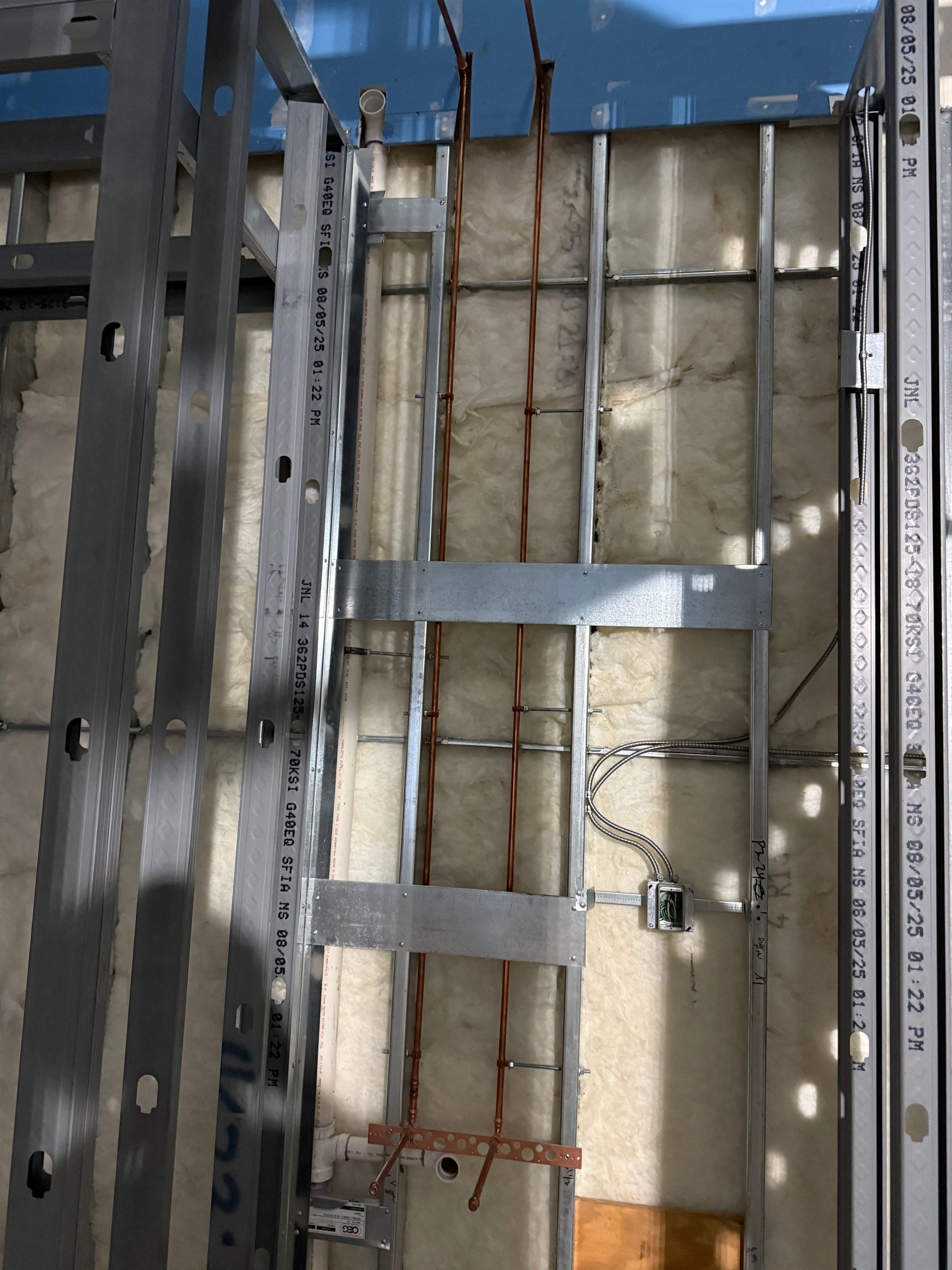 Metal framing with copper pipes and electrical wiring in a wall.