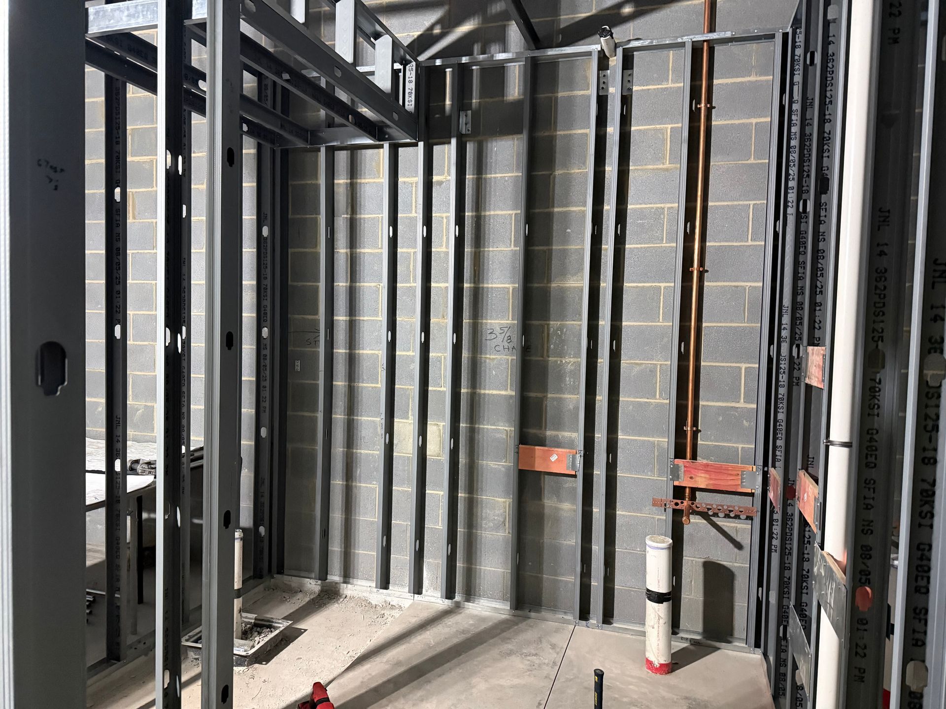 Metal framing inside a room. Exposed cinder block wall with plumbing. Construction site.