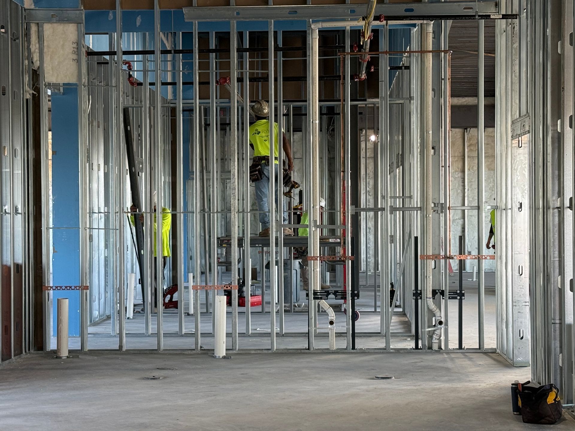Construction workers in high-visibility vests inside a building, working on metal framing.