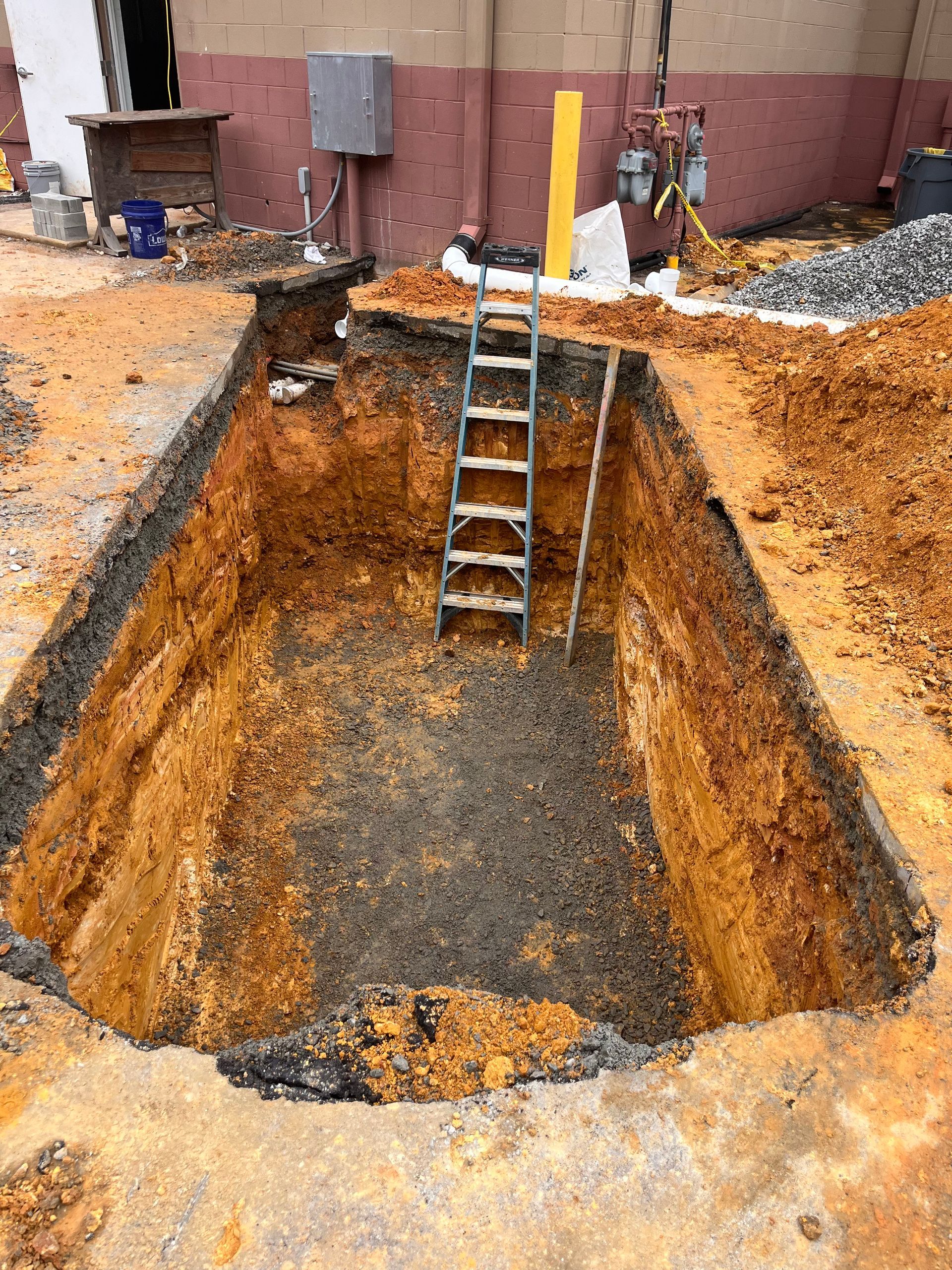 Large excavated rectangular hole with ladder inside; construction site.