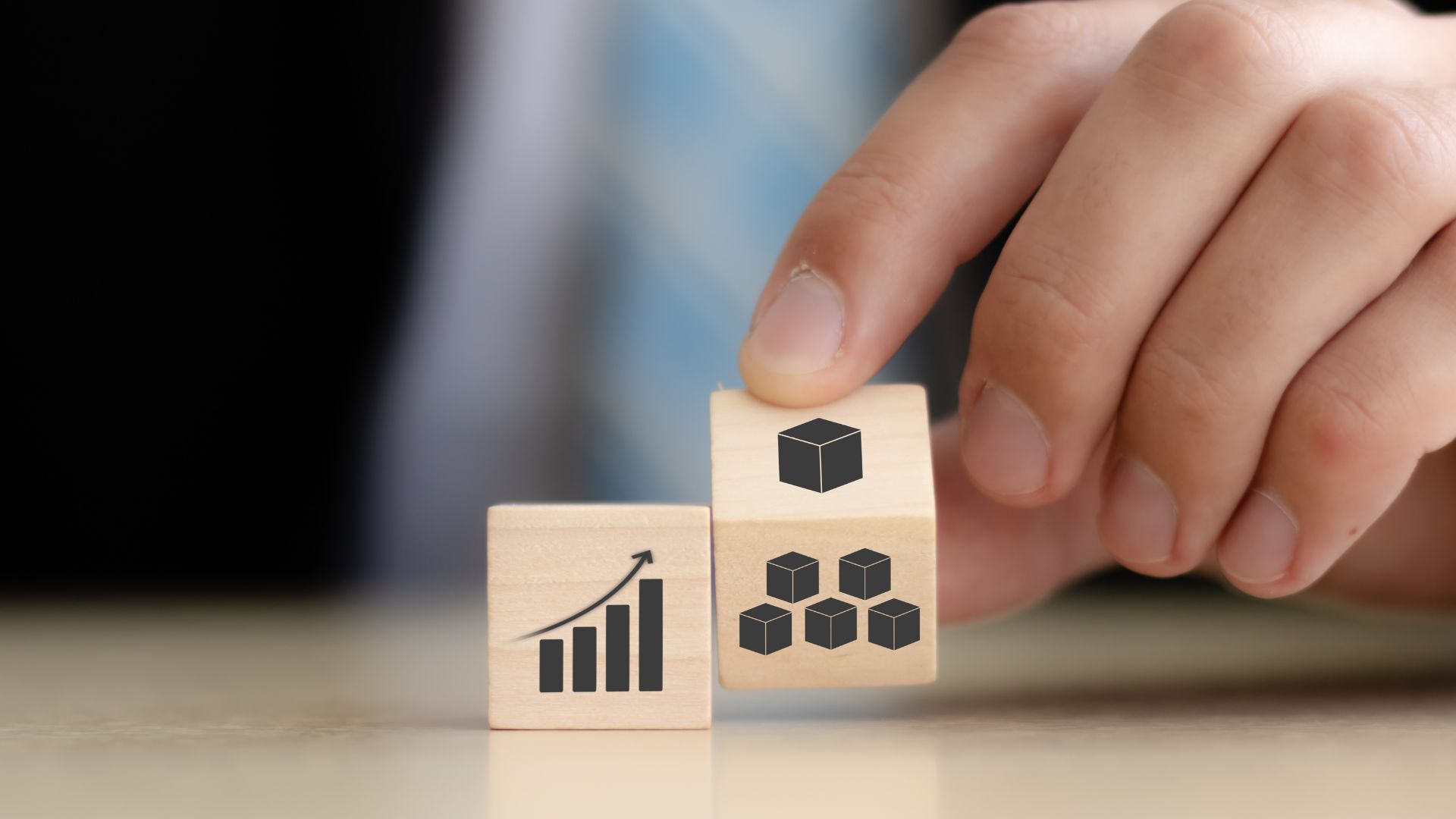 Hand holding a wooden cube with stacked cubes, next to one with a rising bar graph; concept of growth.