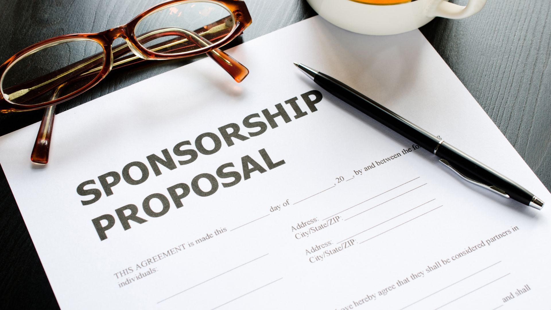 Sponsorship proposal document with eyeglasses and a pen, on a dark surface.