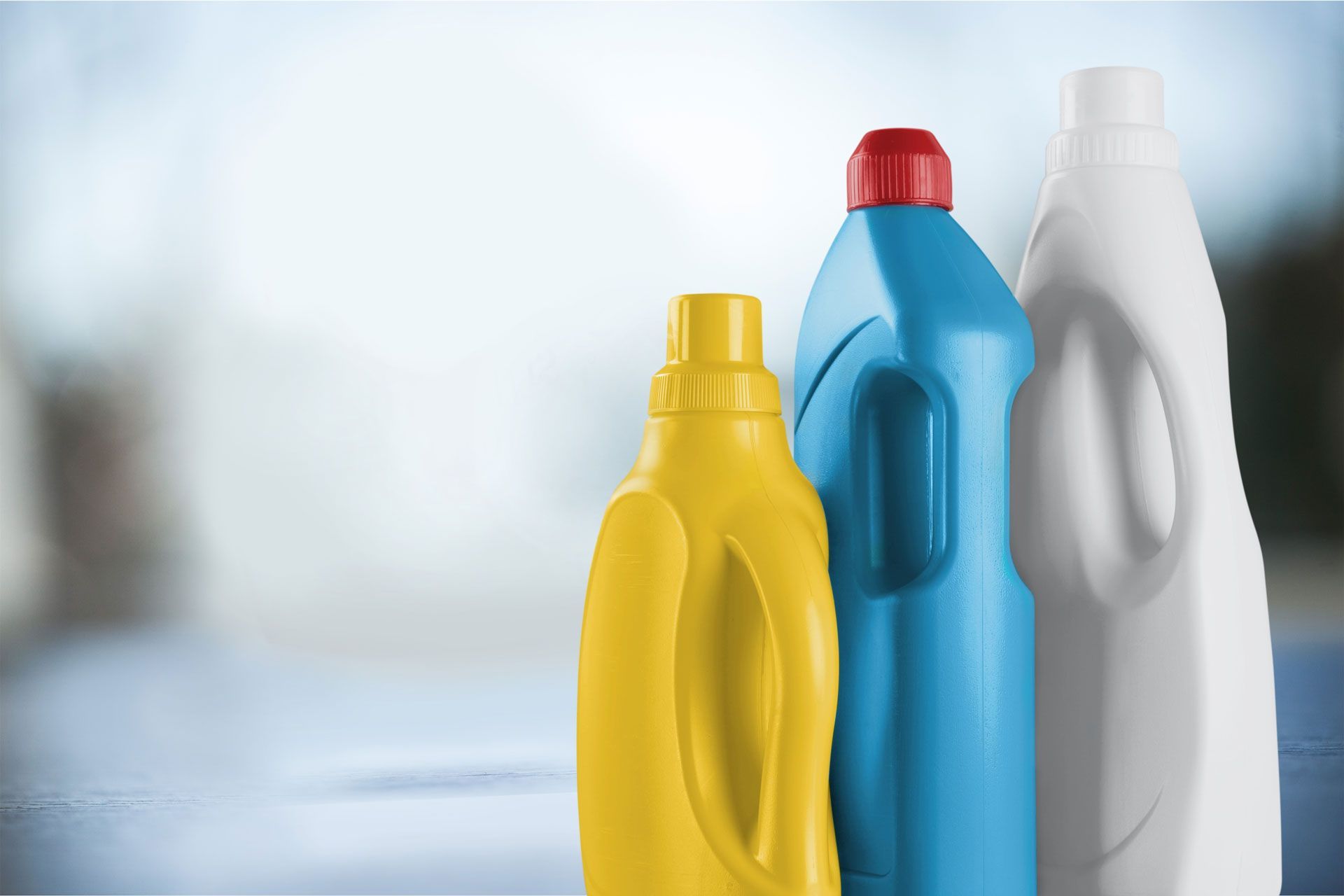 Three plastic detergent bottles in yellow, blue, and white against a blurred background
