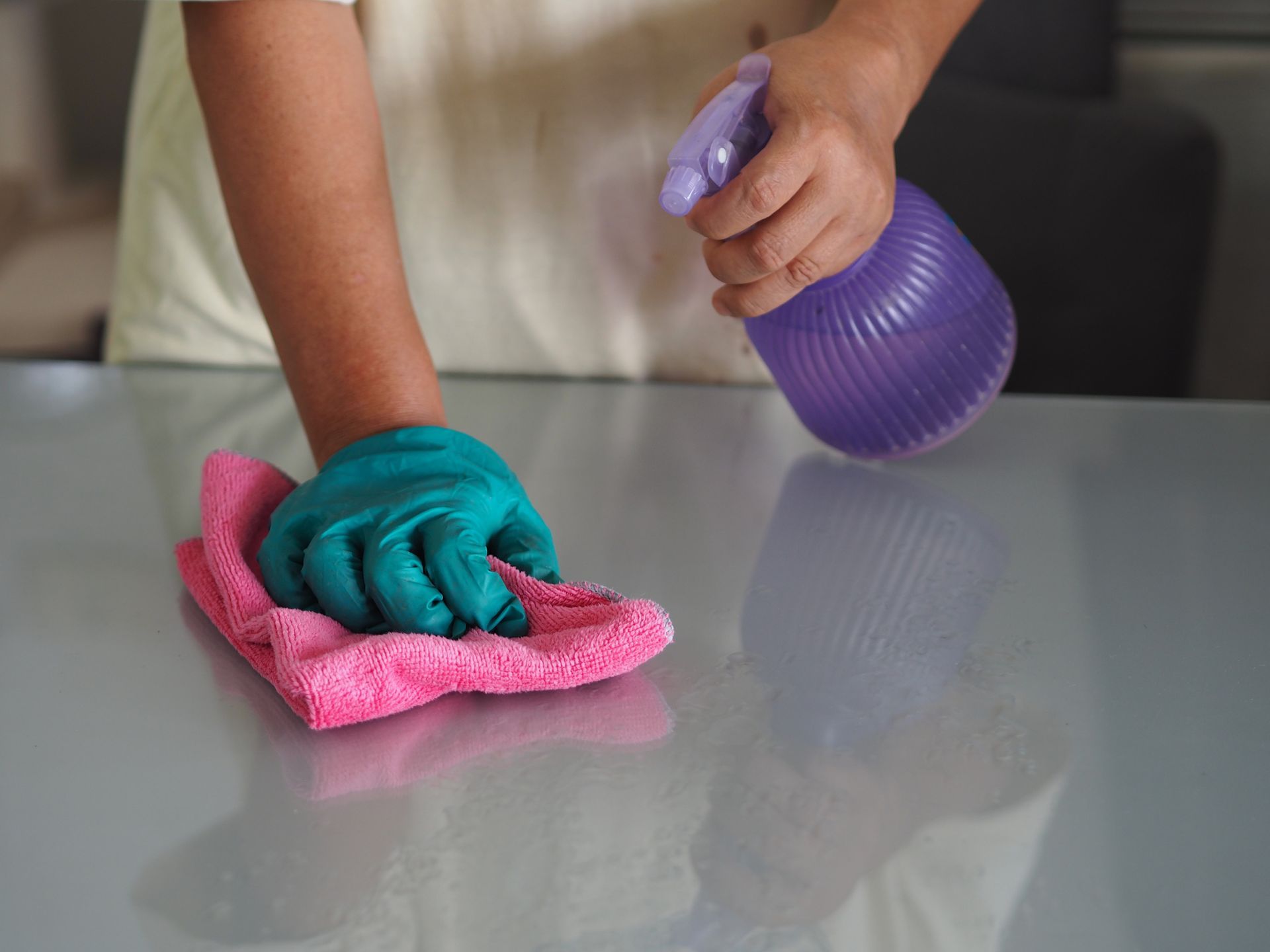 A woman is using a towel and disinfectant to clean a table. A woman is using a towel and disinfectant to clean a table.