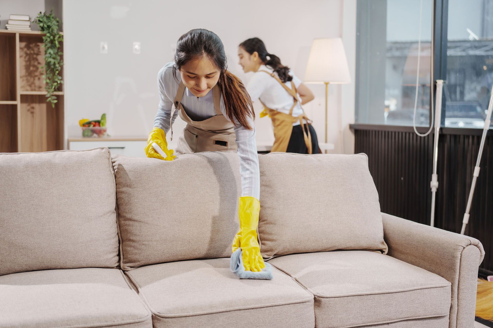 A woman in yellow gloves is cleaning a beige sofa