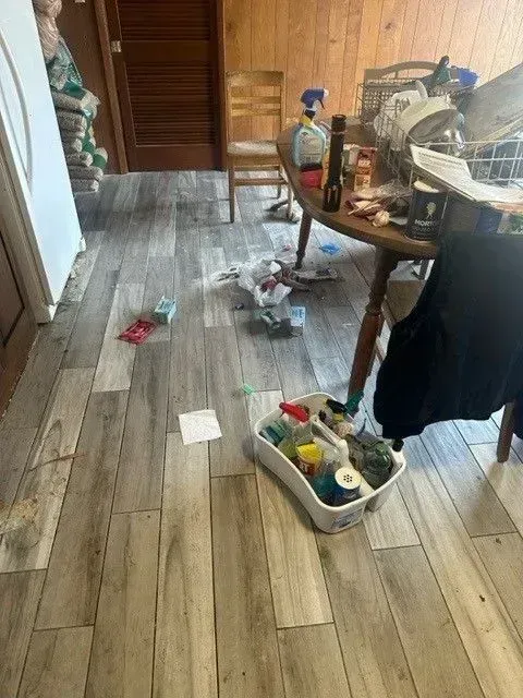 Cluttered kitchen floor with scattered items, cleaning supplies, and a messy table