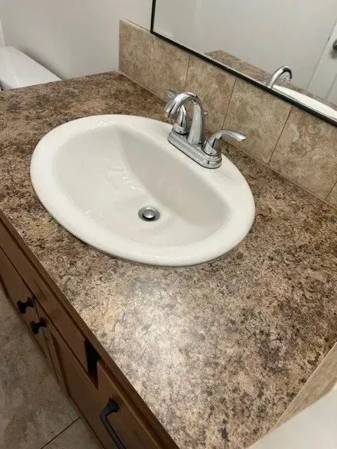 Bathroom vanity with a white oval sink, chrome faucet, and brown countertop