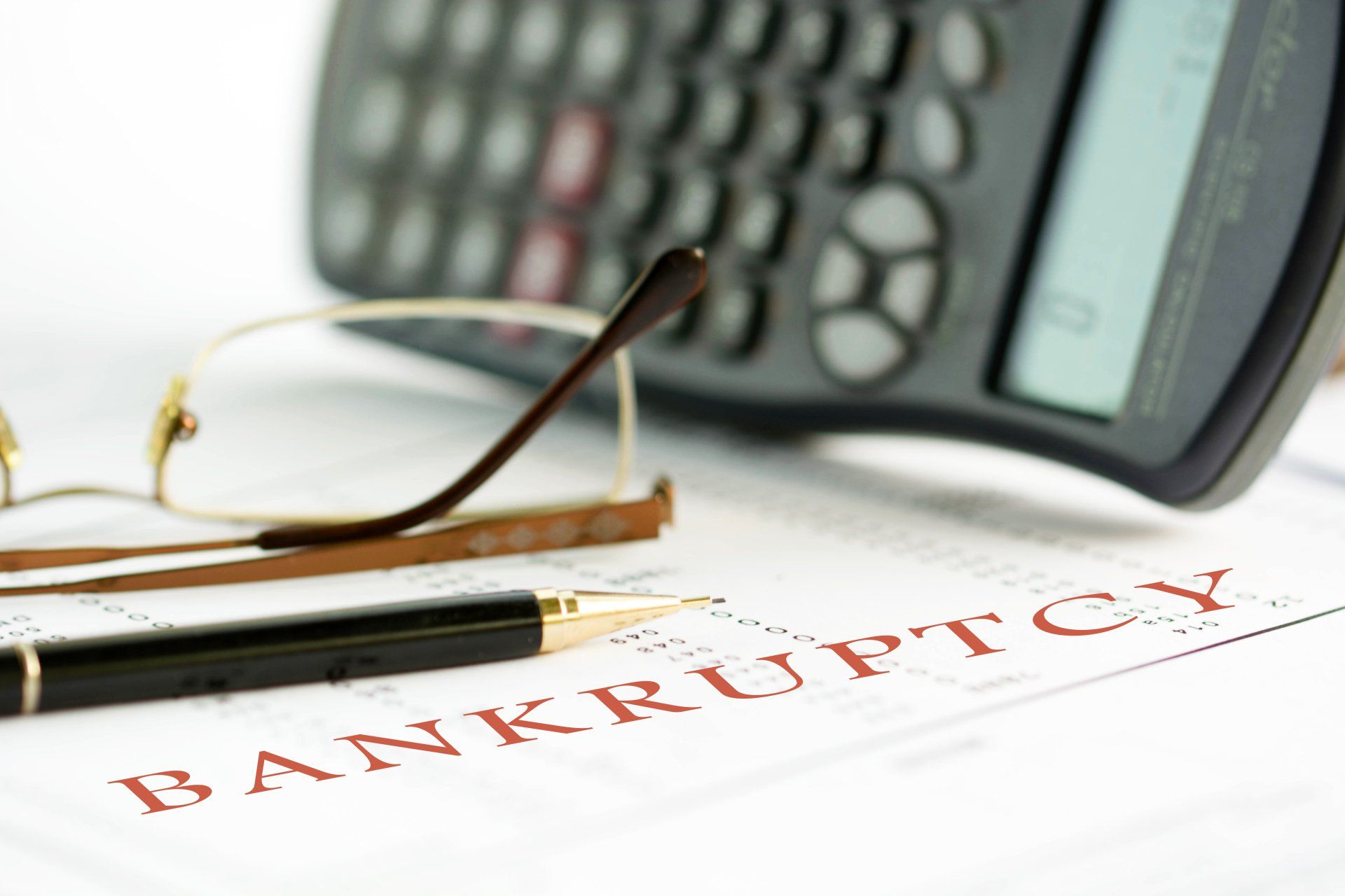 Bankruptcy concept image of a pen, calculator and reading glasses on financial documents.
