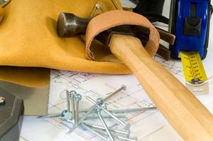 A hammer is sitting on top of a drawing next to a tape measure