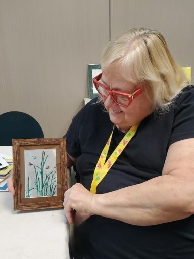 A community member holding their own painting from the art & ceramic studio 