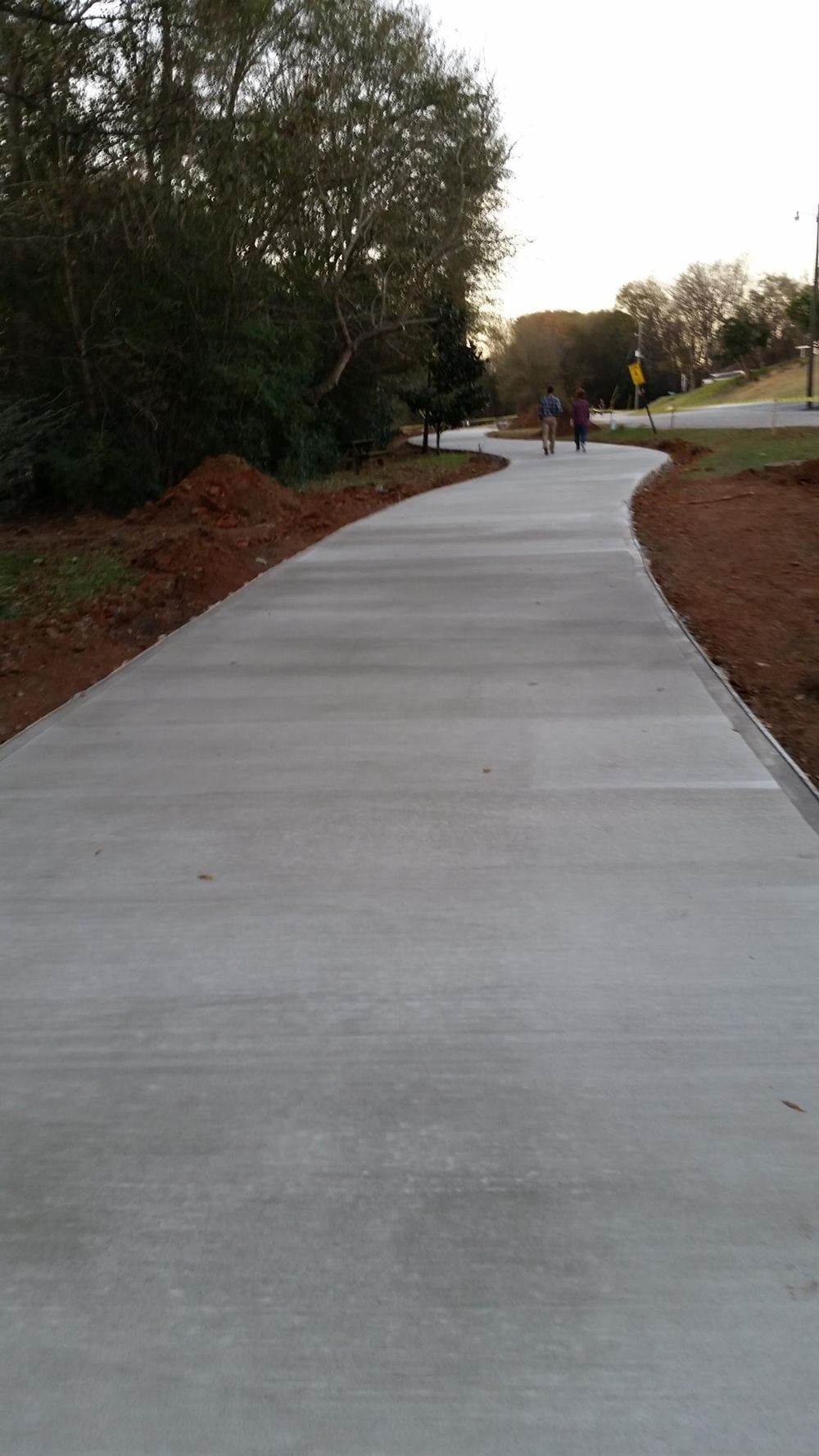 A person is walking down a concrete driveway surrounded by trees.