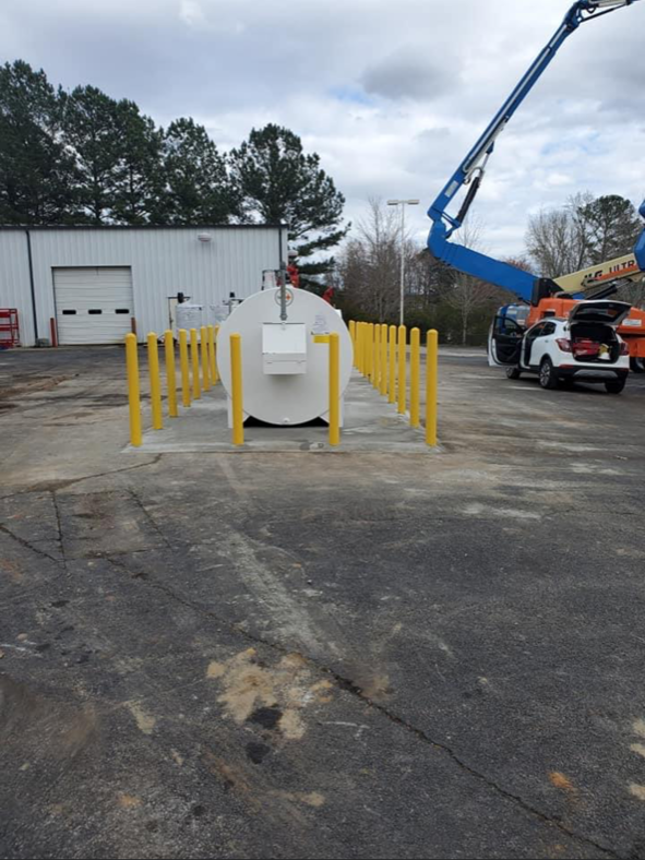 A white tank is surrounded by yellow poles in a parking lot
