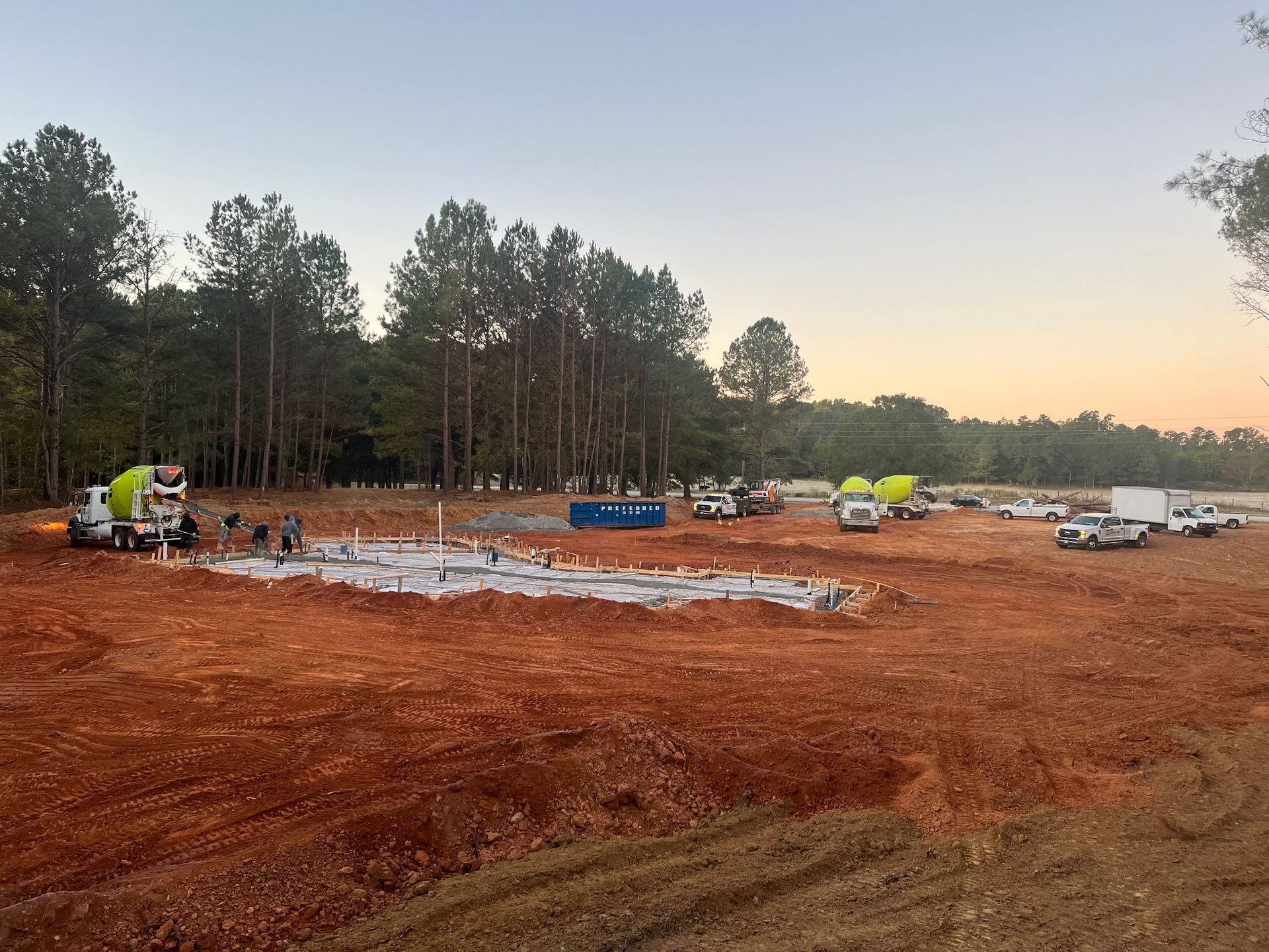 A construction site with a lot of trucks and trees in the background.