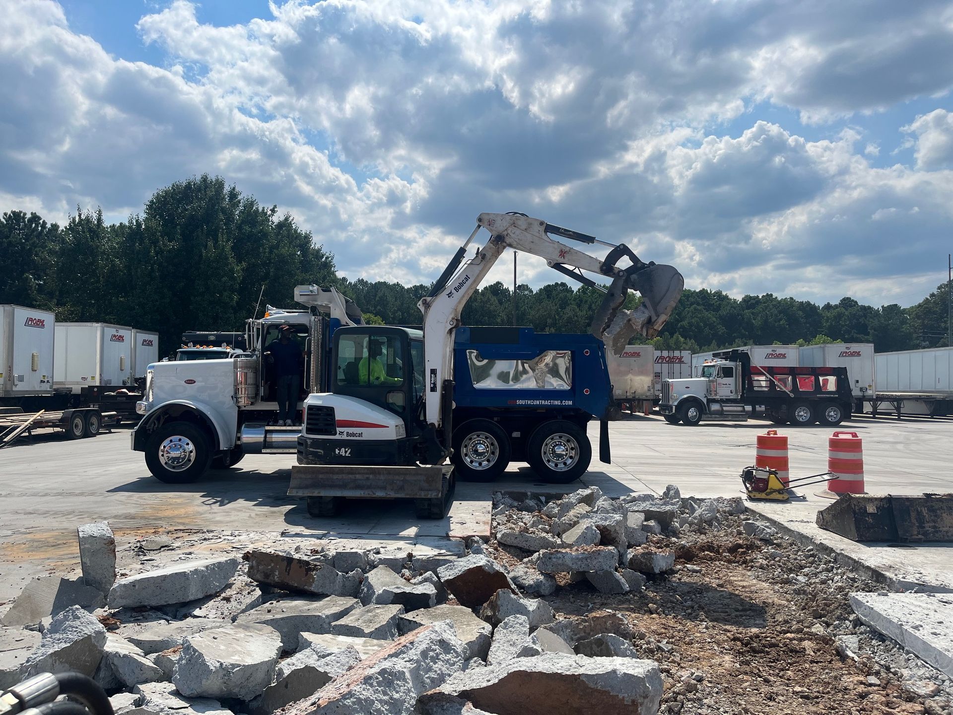 An excavator is loading rocks into a dumpster in a parking lot