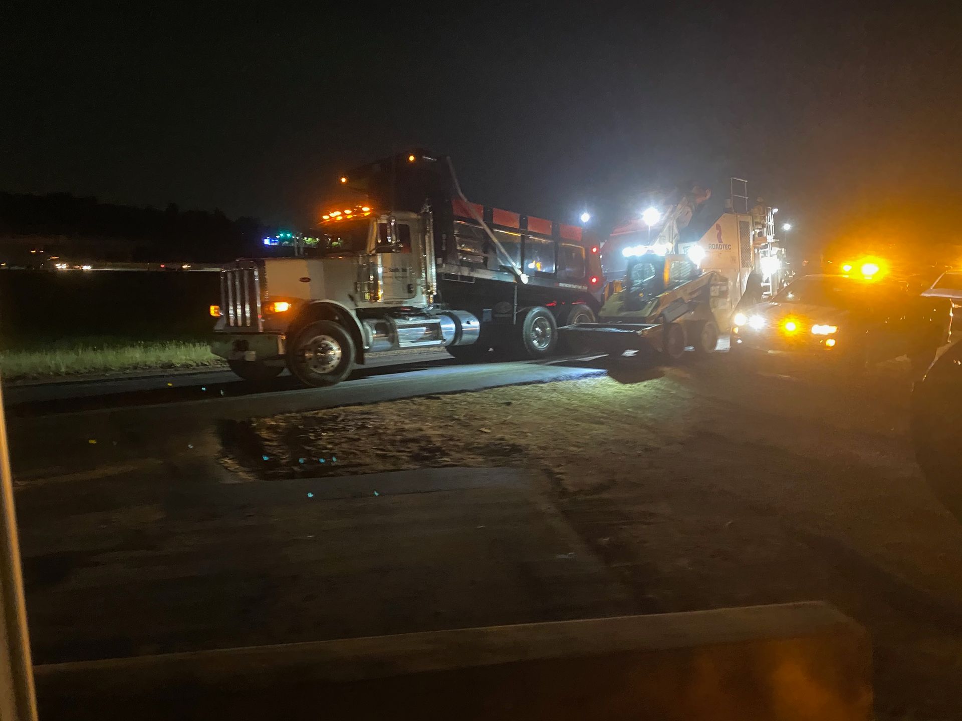 A tow truck is towing a car at night in a parking lot.