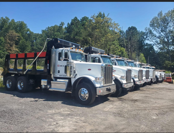 A row of dump trucks are parked in a parking lot.