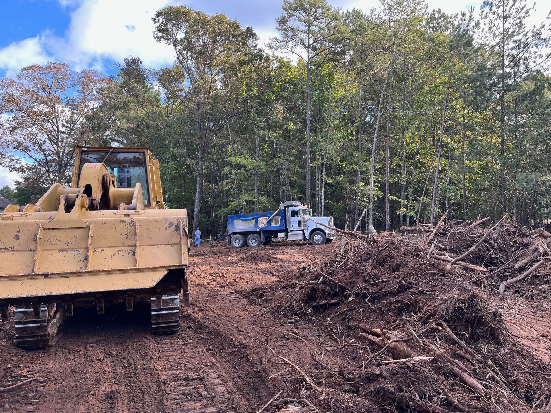 A bulldozer is driving down a dirt road next to a truck.