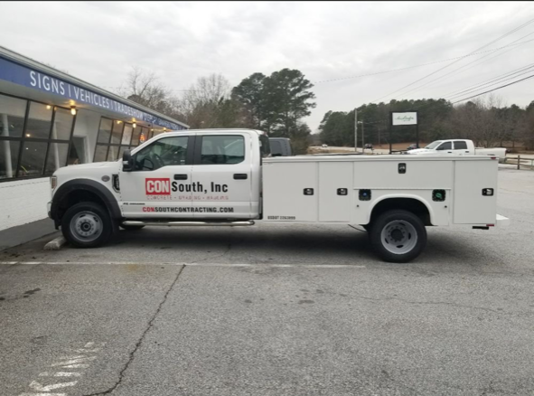 A white truck is parked in front of a building that says signs