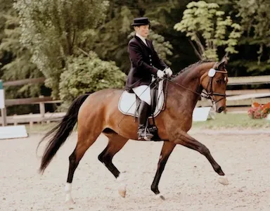 Eine Frau mit schwarzem Hut reitet auf einem braunen Pferd
