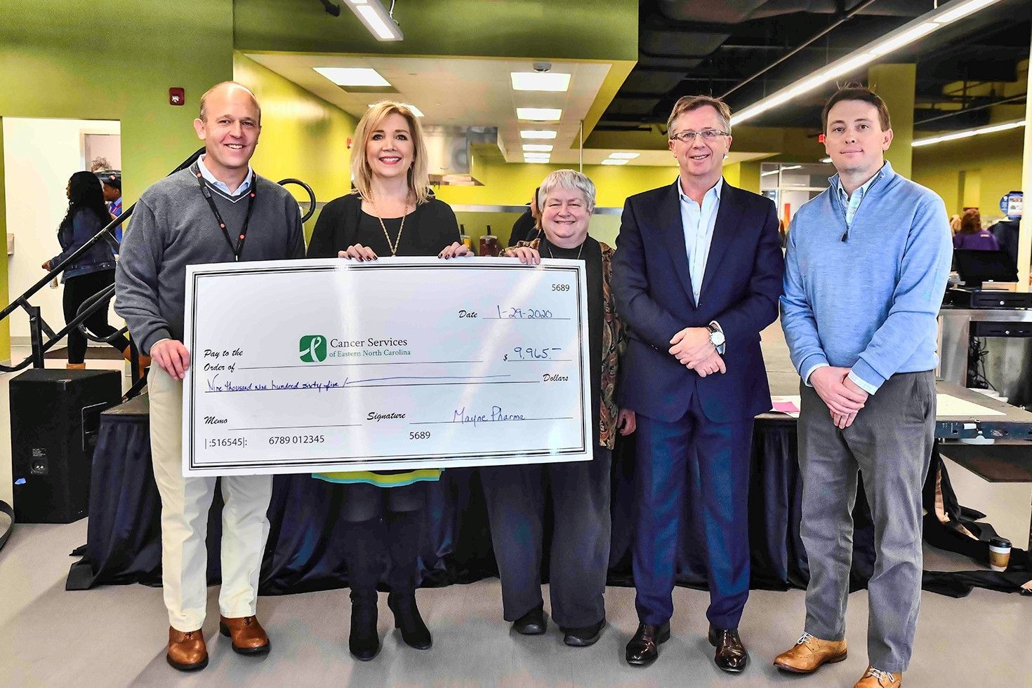 a group of people standing next to each other holding a large check .