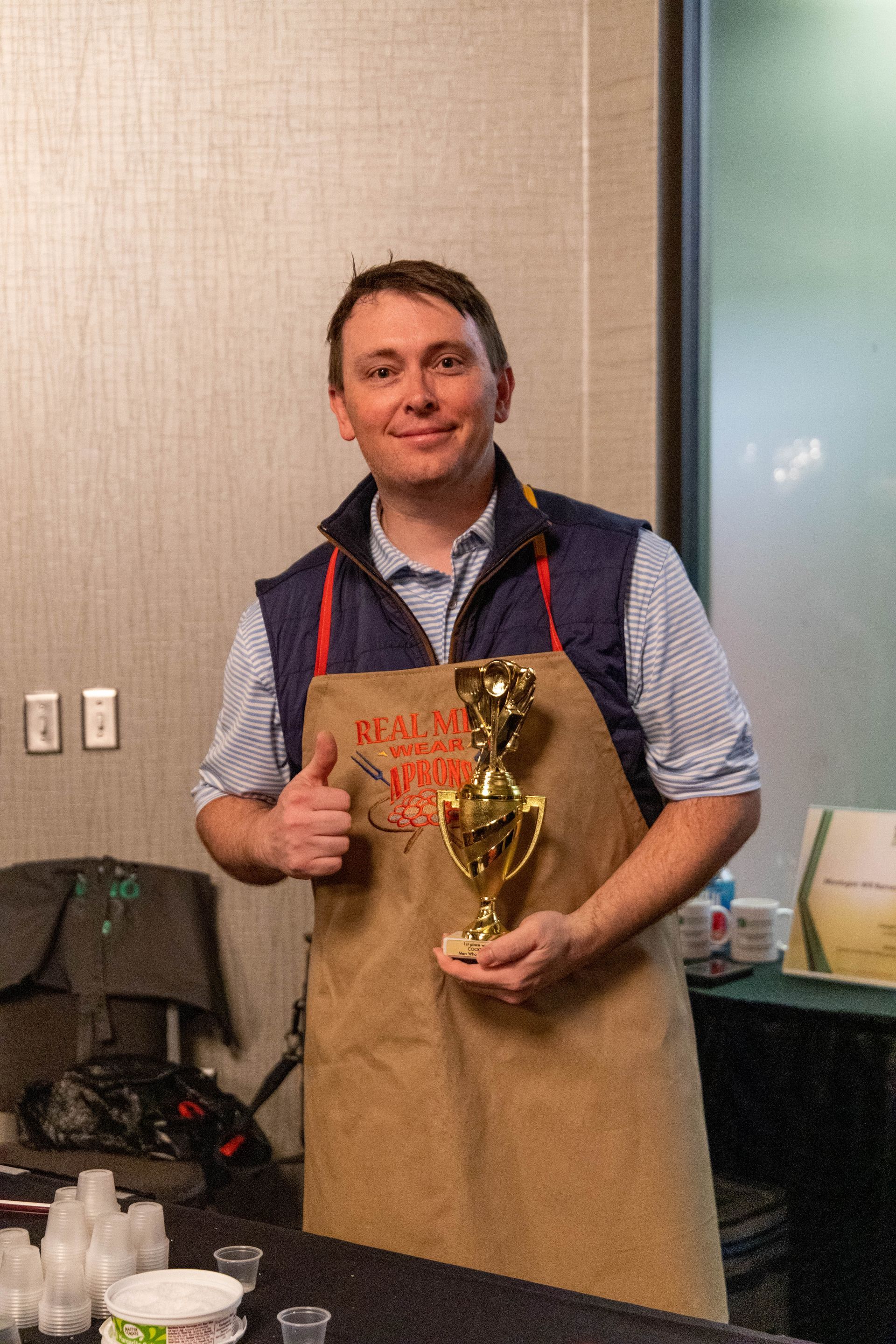 a man in an apron is holding a trophy and giving a thumbs up .