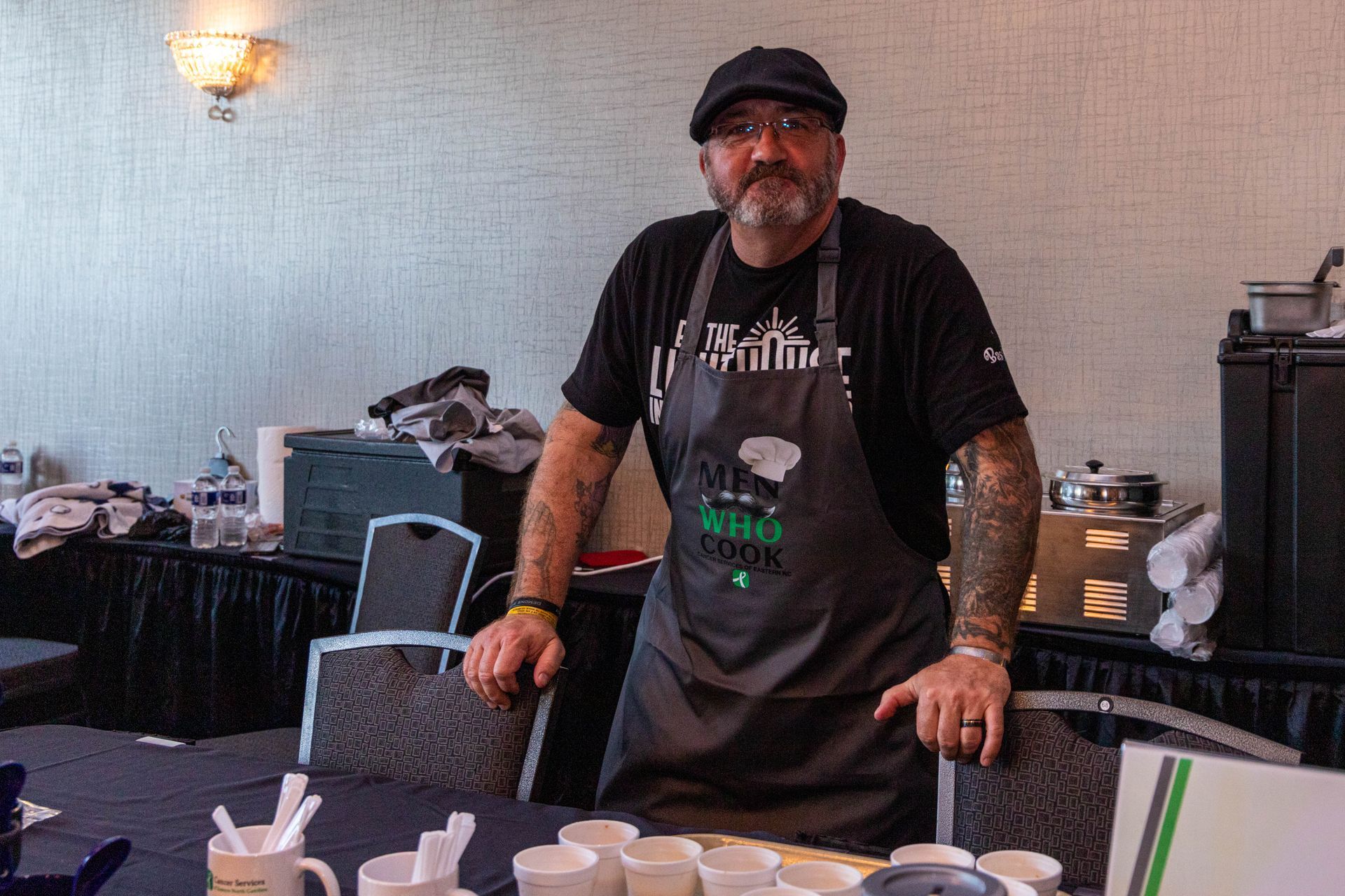 a man in an apron is standing in front of a table .