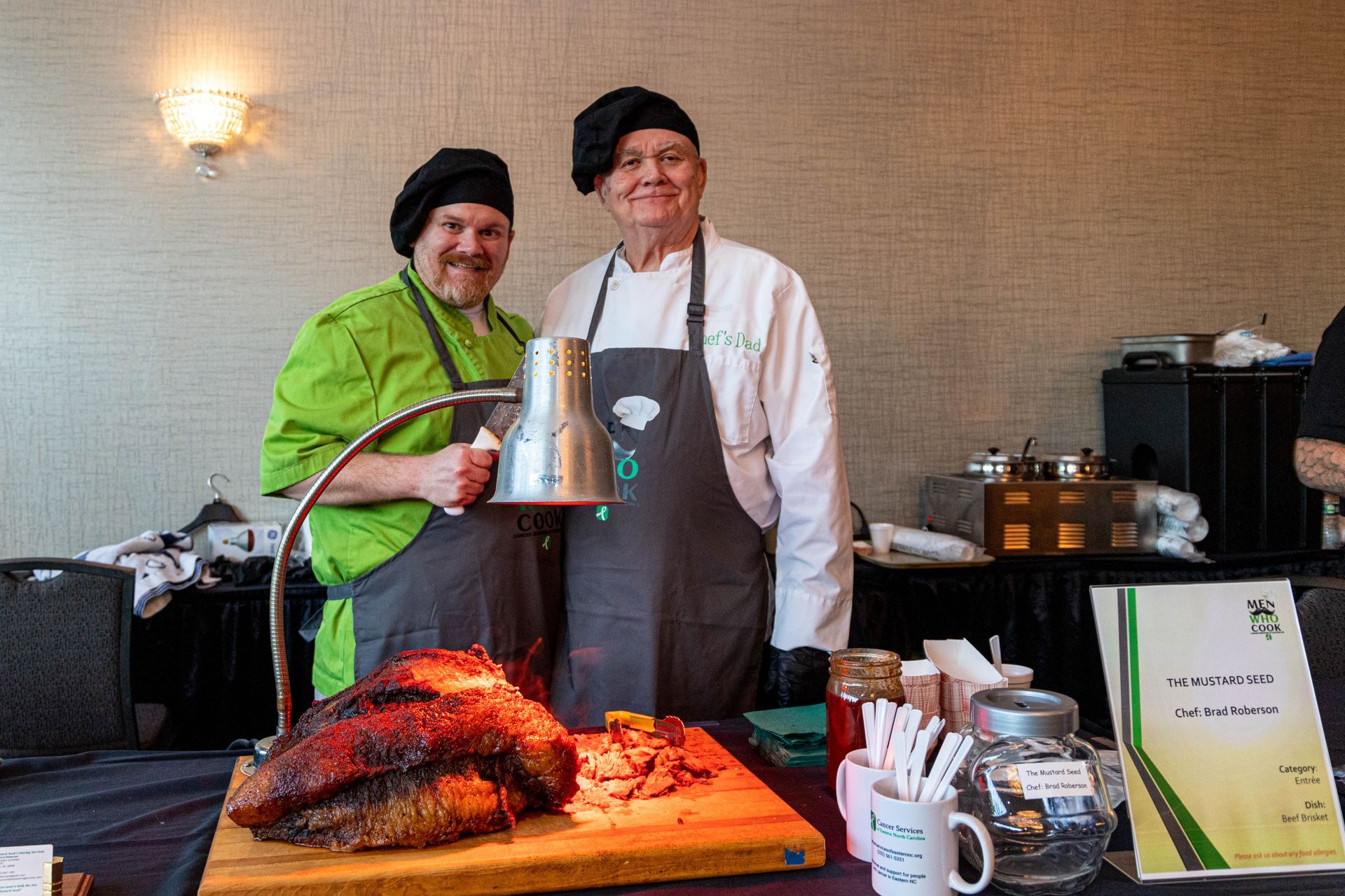 two chefs are standing next to a large piece of meat on a cutting board .