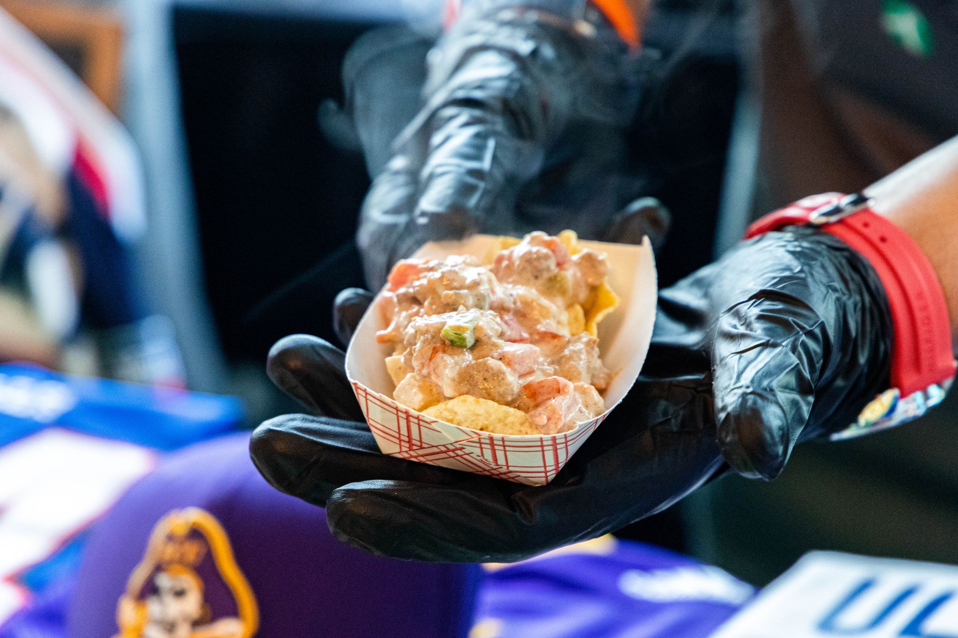 a person wearing black gloves is holding a container of food in their hand .