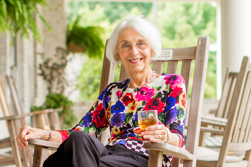 an elderly woman is sitting in a rocking chair holding a glass of tea .