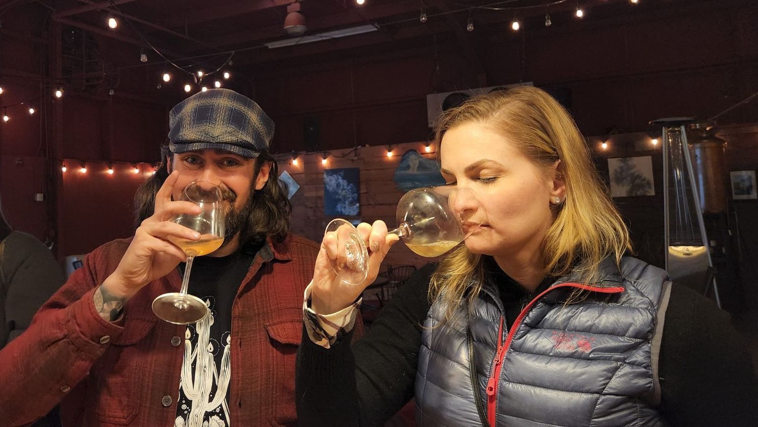 Two people having a tasting flight of mead: one person smiling at the camera, the other appreciating the aromatics.