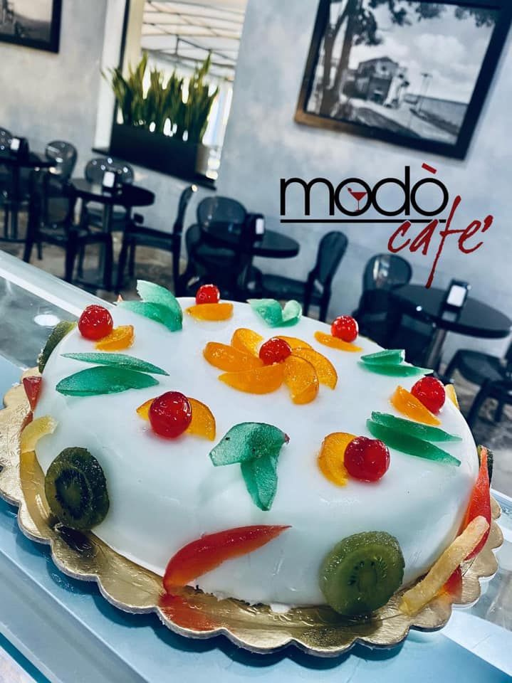 Una torta rotonda ricoperta di glassa bianca, decorata con ciliegie rosse brillanti e fette di arancia candita, servita in un caffè.