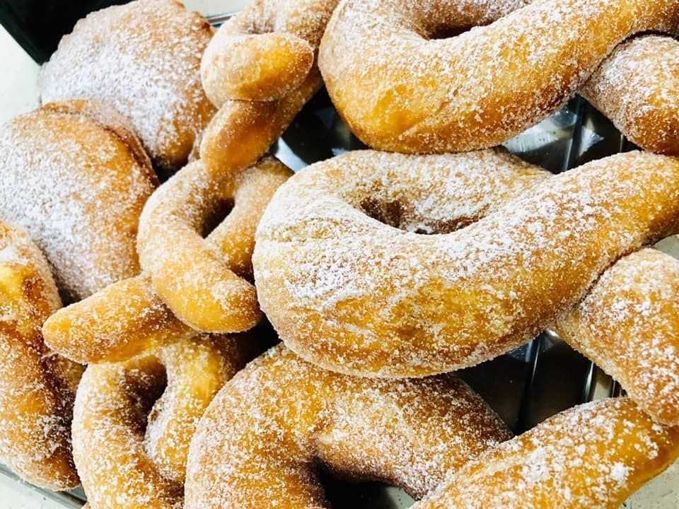 Una pila di pasticcini dorati, attorcigliati e simili a ciambelle, generosamente spolverati di zucchero a velo bianco.