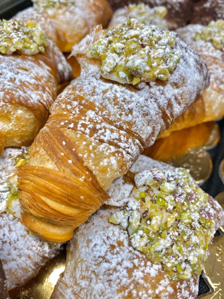Un primo piano di pasticcini dorati e friabili, spolverati di zucchero a velo e guarniti con pistacchi tritati.