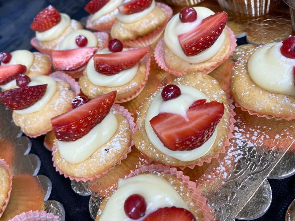 Un gruppo di piccole tortine dorate, ricoperte di glassa cremosa, fettine di fragole fresche e un singolo ribes rosso.