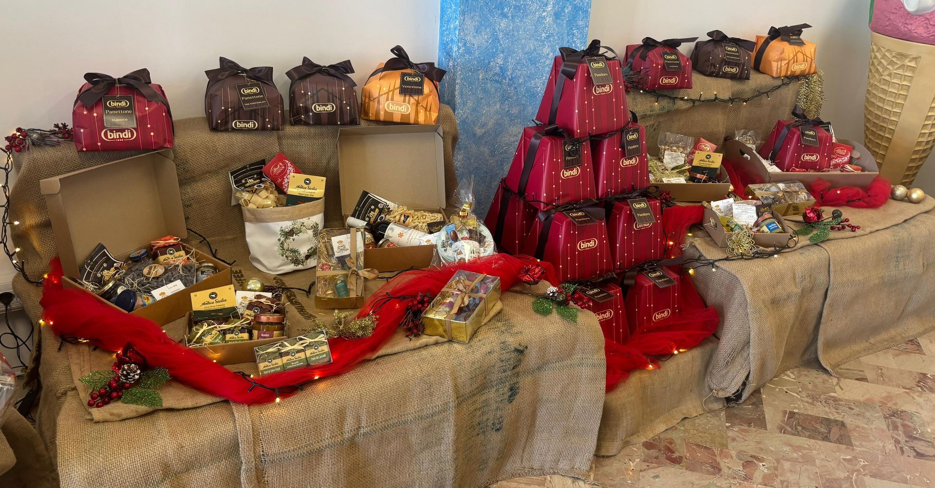 Una composizione di scatole regalo e pacchetti incartati nei toni del rosso, del marrone e dell'oro, disposti su superfici rustiche di tela di iuta.