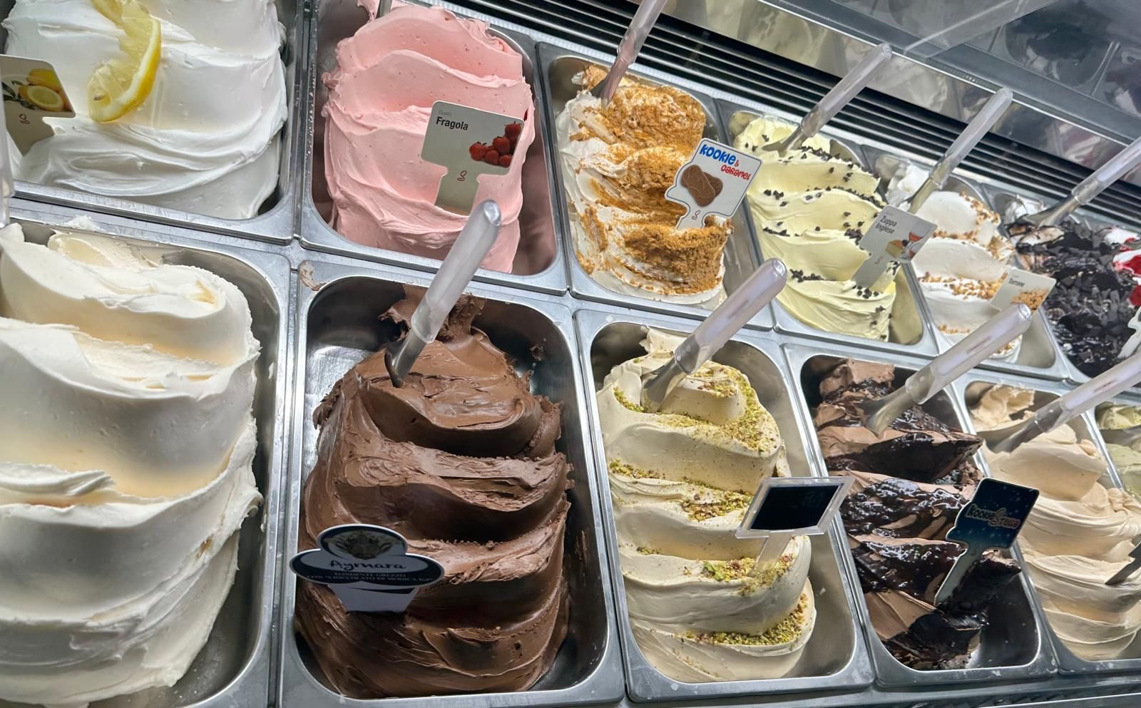 Una vetrina con due file di palline di gelato di vari colori, ciascuna etichettata con un piccolo cartellino.