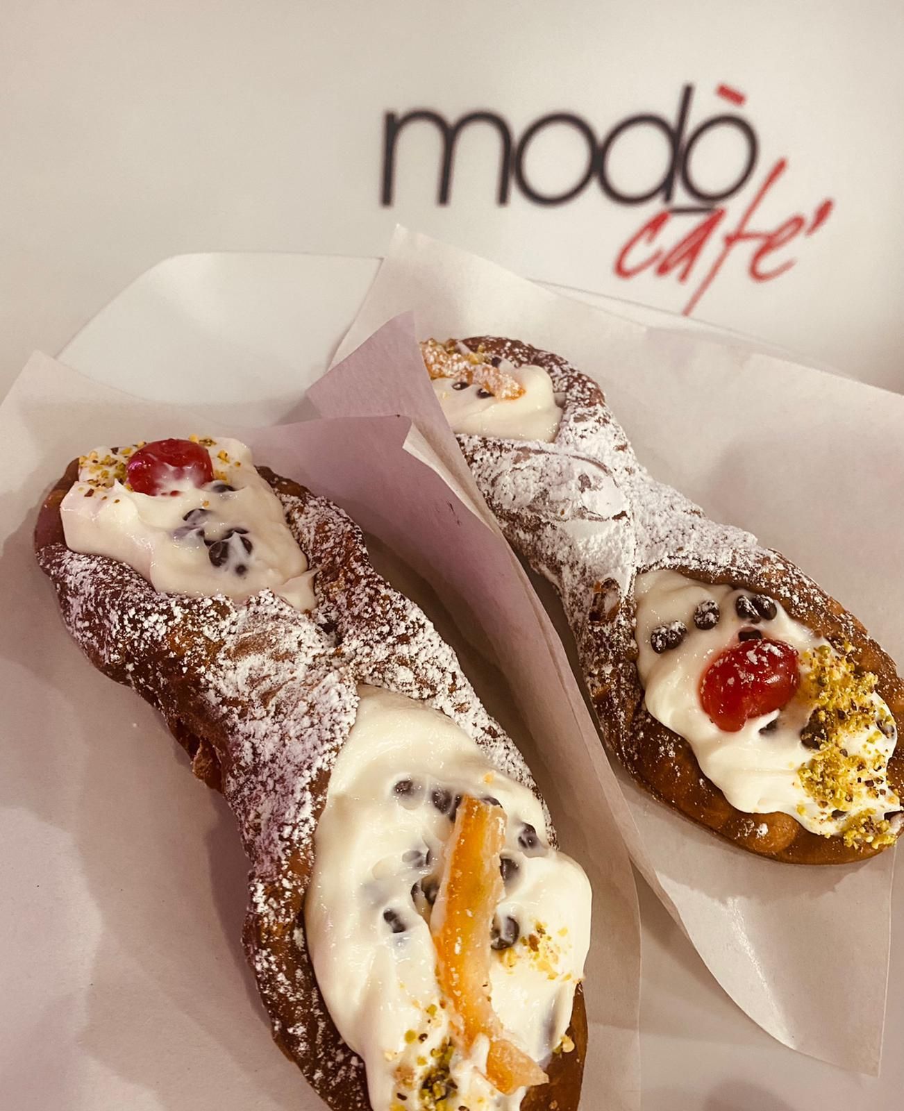 Cinque cannoli allineati diagonalmente su una superficie grigia, ripieni di crema e guarniti con pistacchi tritati e zucchero a velo.