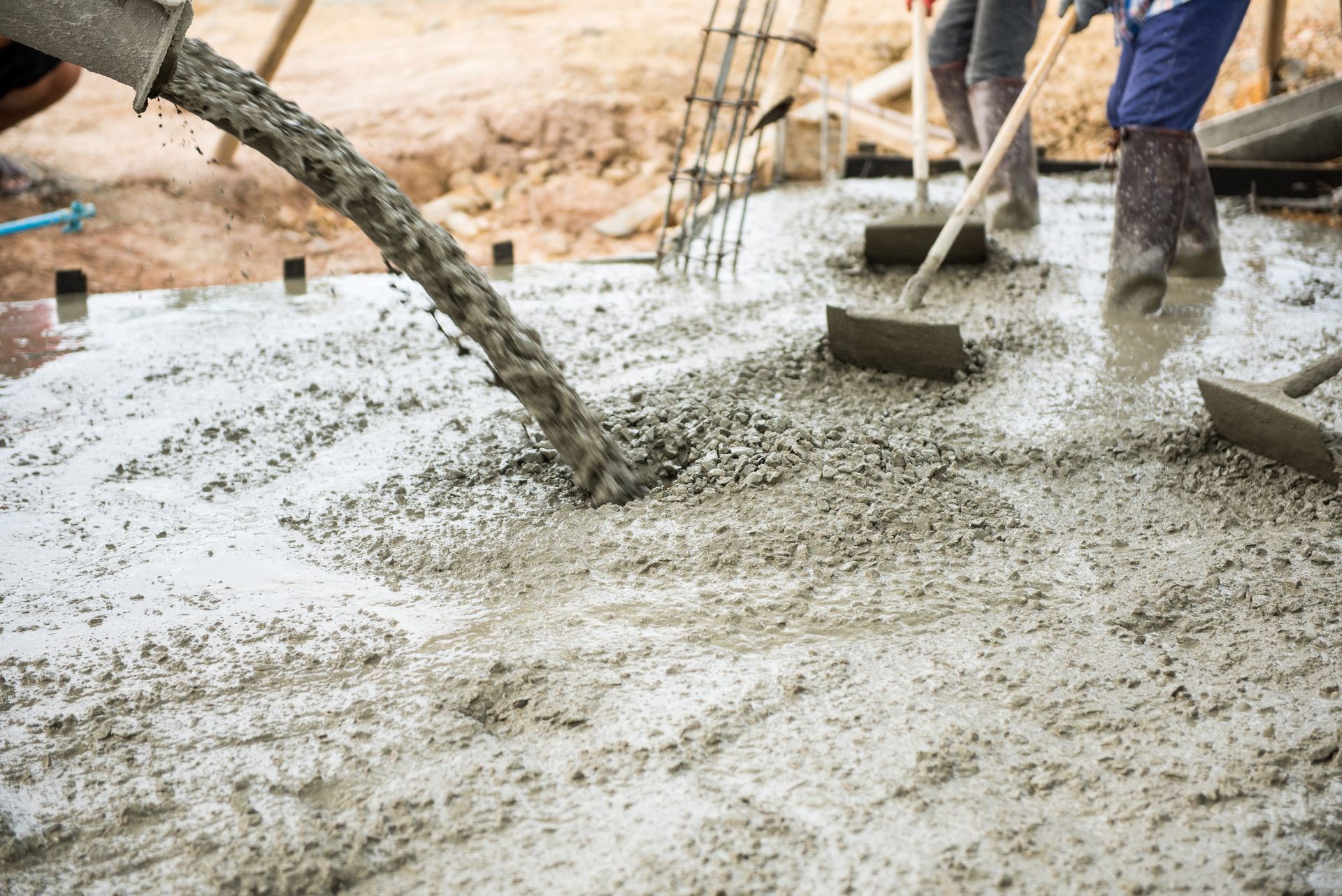 A man wearing orange gloves is using a trowel to spread concrete on a floor.