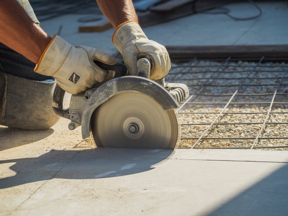 Person wearing gloves using a circular saw to cut through concrete on a construction site.