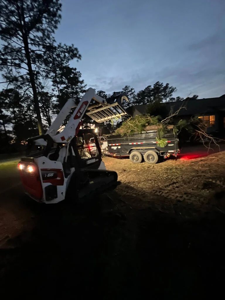 A bobcat is loading trees into a trailer at night.