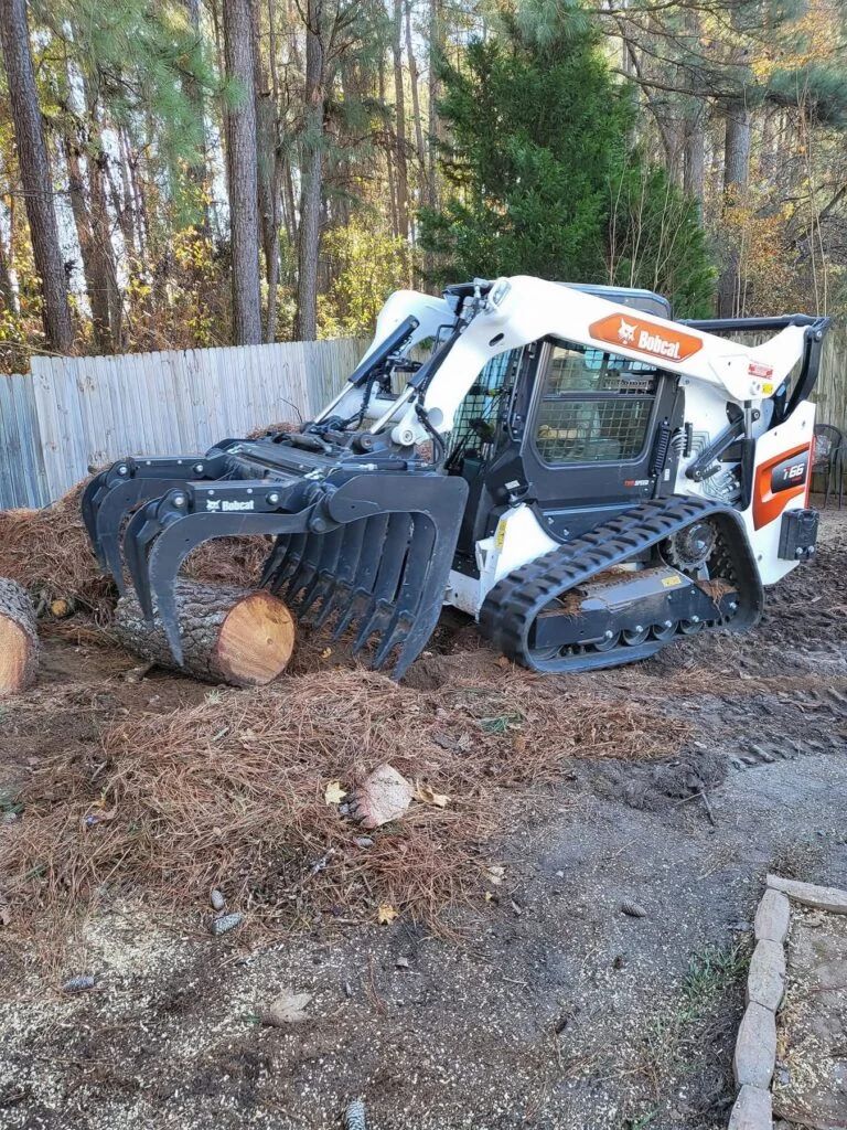 A bobcat is sitting in the dirt next to a pile of wood.