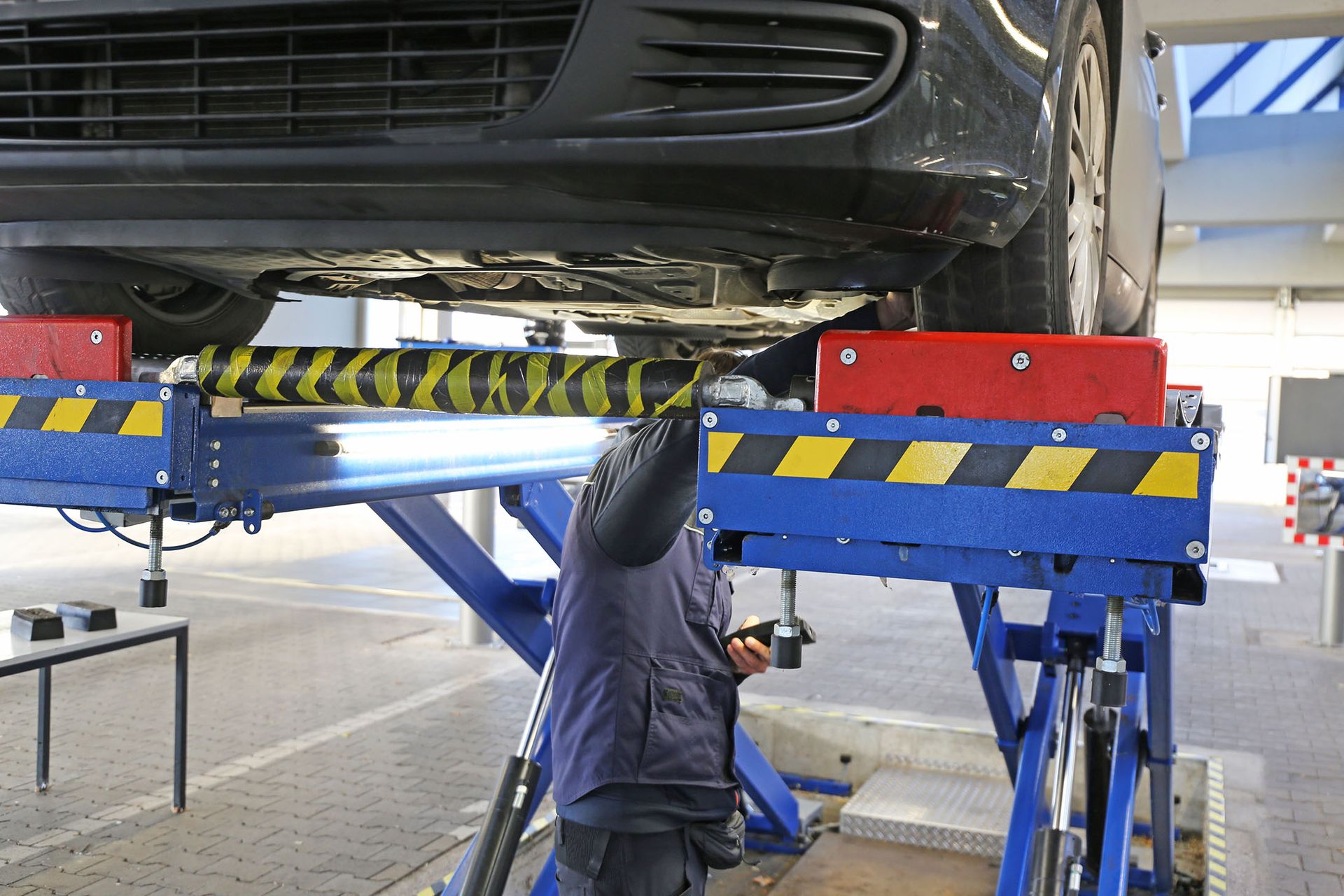 Ein Mann arbeitet in einer Garage auf einer Hebebühne an einem Auto.