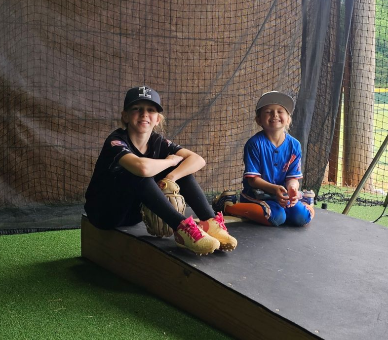 Two children sitting on a raised platform inside a netted indoor play area.