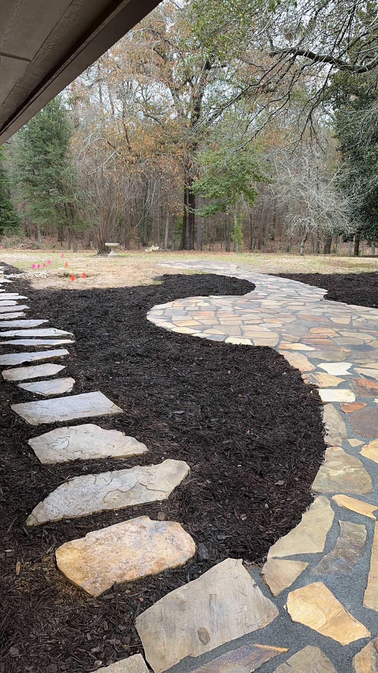 A stone walkway leading to a patio with trees in the background.