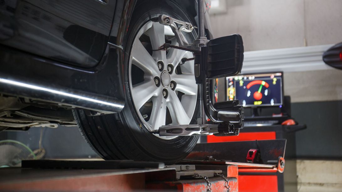 A car wheel mounted on a professional alignment machine with a computer display in the background showing data. | John’s Auto Center