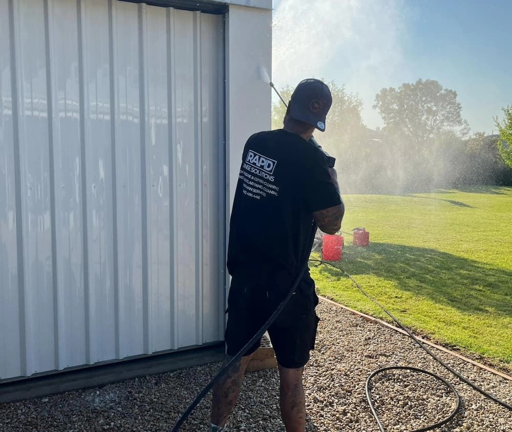 Man Power Washing a White Corrugated Metal Building Exterior — Rapid Rinse Solutions in Katunga, VIC