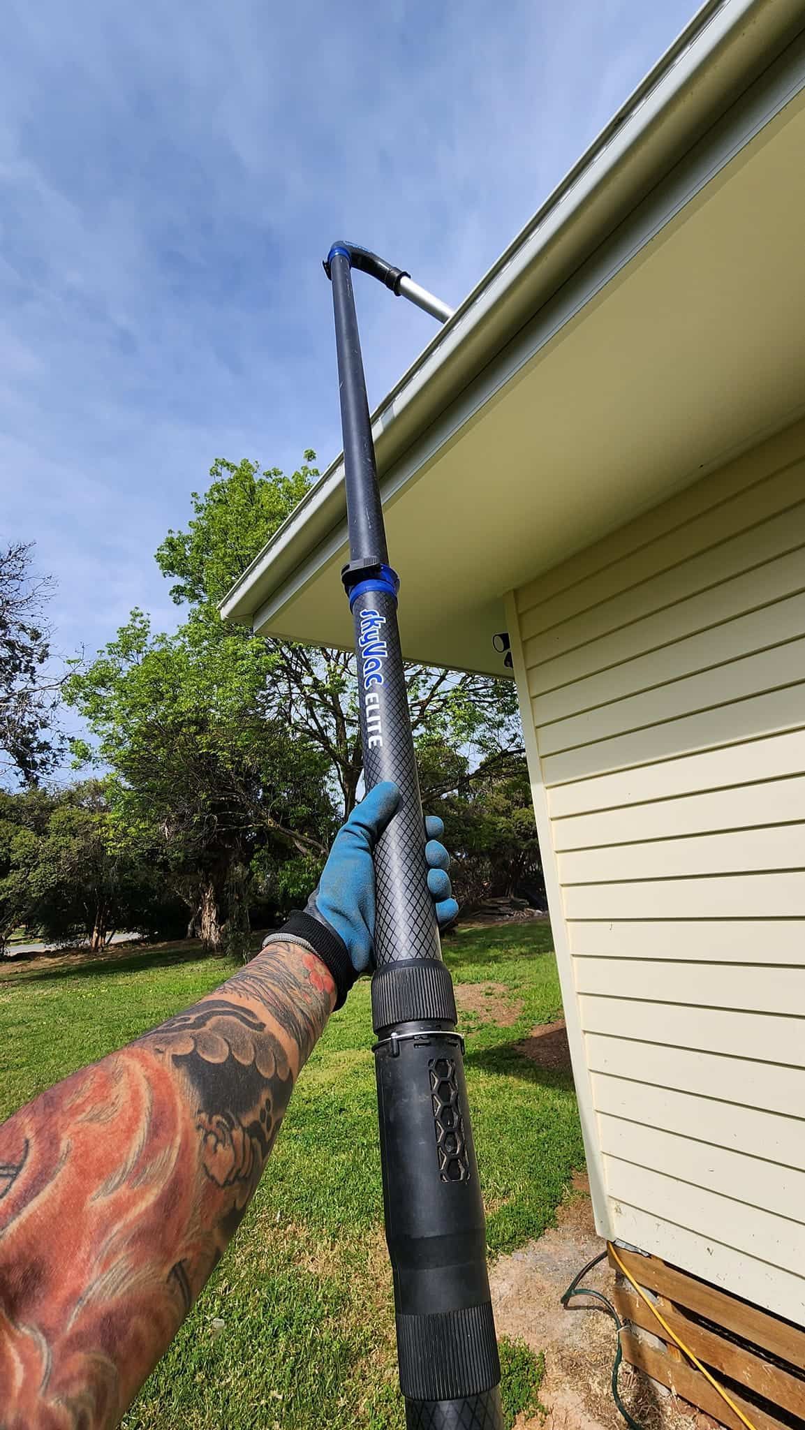 Person With Tattoos Using a Long Tool to Clean Gutters on a House — Rapid Rinse Solutions in Yarrawonga, VIC
